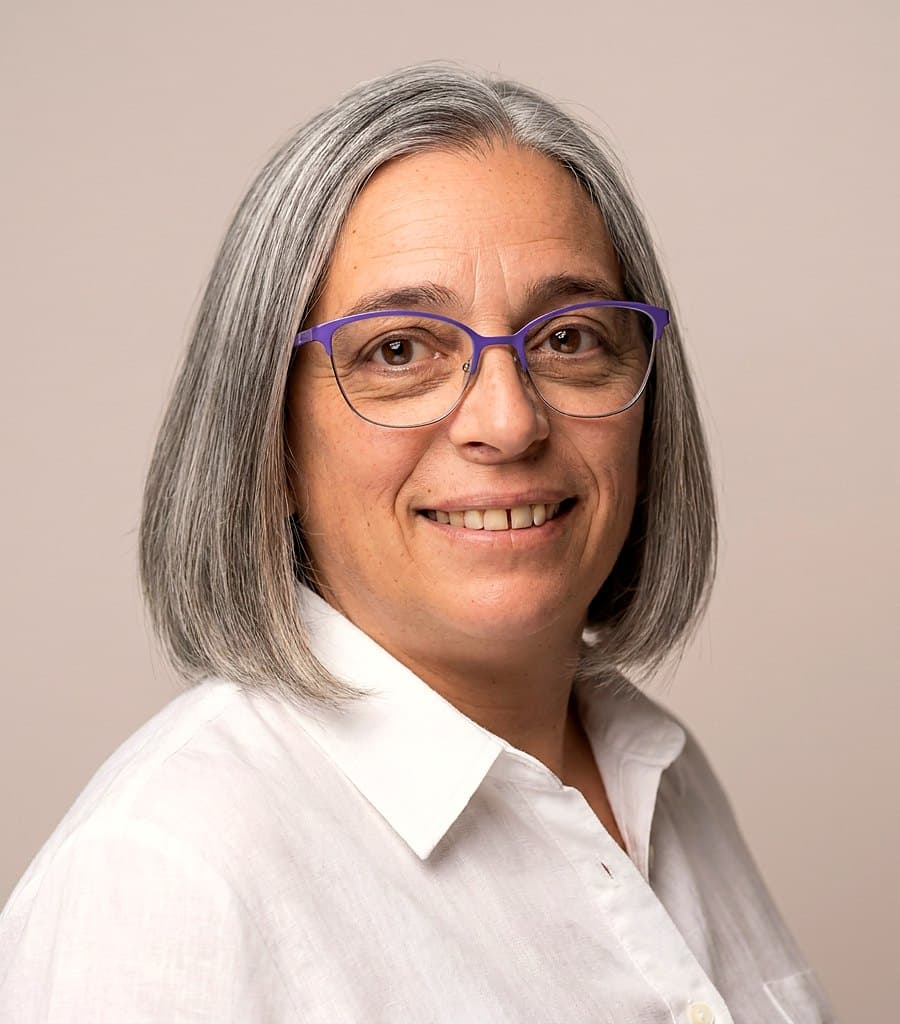 Kiki, asesora de viajes, sonriendo con anteojos violetas y camisa blanca